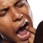 Pessoa preocupada descobrindo verruga na boca, sintoma de papiloma oral possivelmente causado por HPV