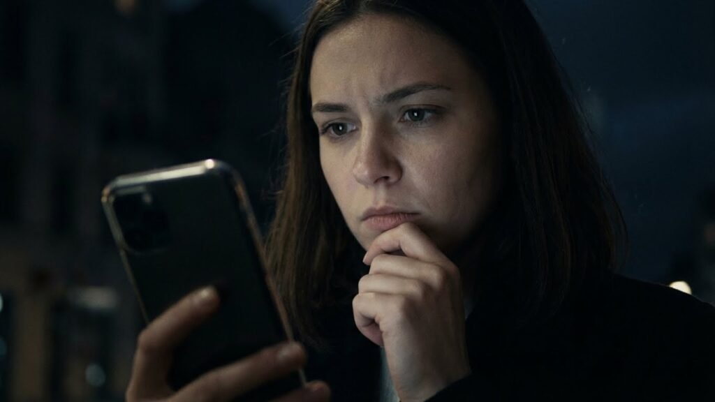 Mulher com a mão no rosto e celular na outra mão, com expressão decidida, procurando um dentista para a dor do siso.